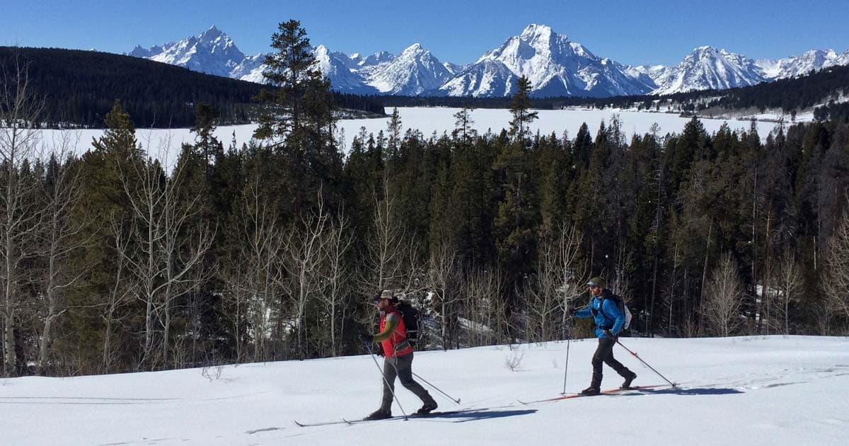 Two men cross country skiing with a view of the Teton Mountains in the background on a sunny Winter day in Wyoming.