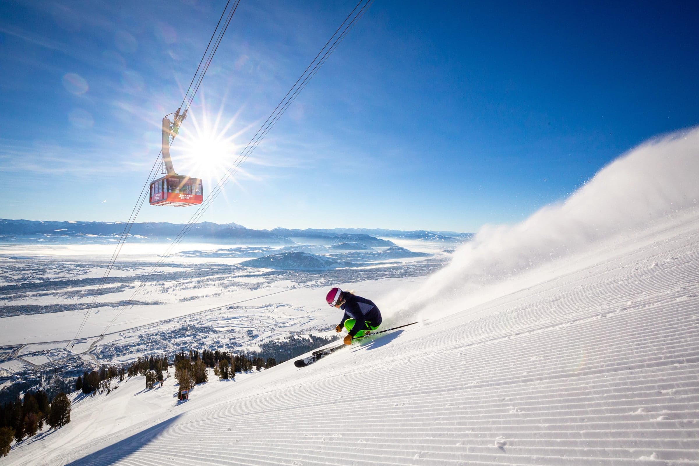 A skier heading down the slope with a gondola overhead in Jackson Hole.